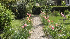 Un sendero en un jardín bordeado de tulipanes rosados y diversas plantas, que conduce a un edificio con fachada de ladrillo.