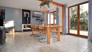 A dining area with a wooden table and chairs, a large window with curtains, and a view of greenery outside. - Amazing home in Mejannes le Clap (Mejannes le Clap)