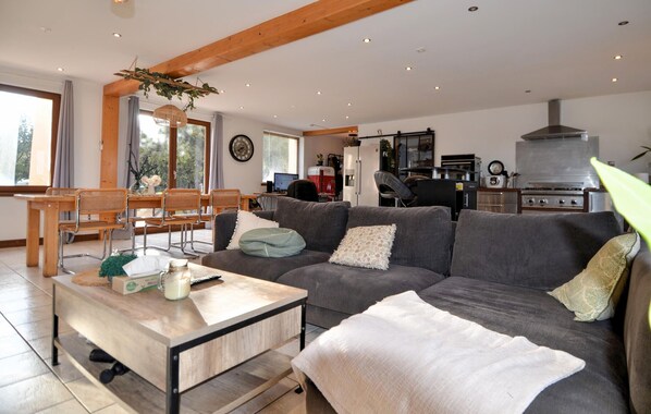 A spacious living area with a large gray sofa, a wooden coffee table, and a dining table with chairs.