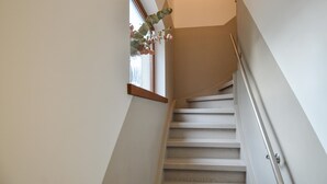 A staircase with a handrail, a window with a plant, and a door at the top.