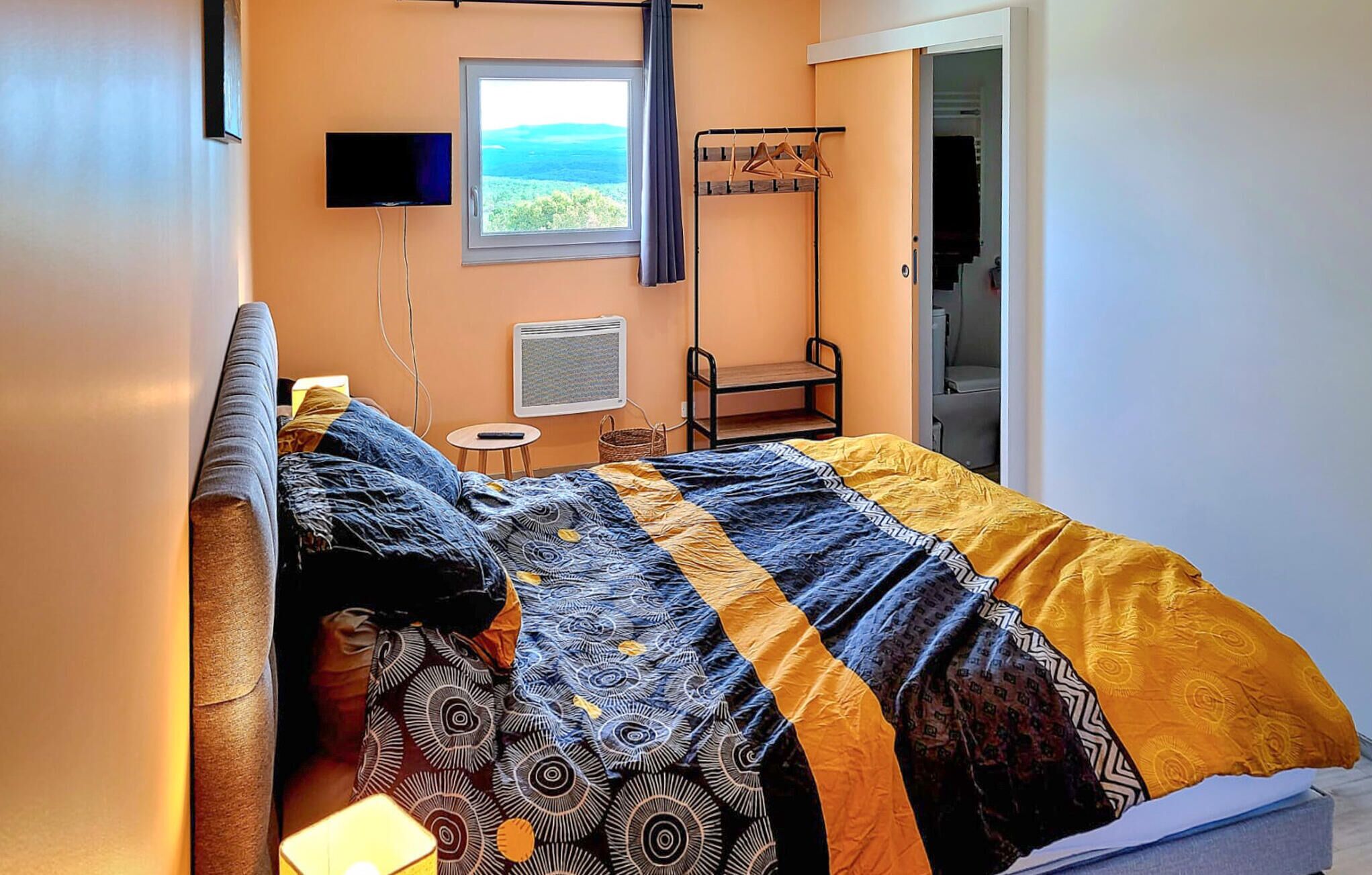 Ein Schlafzimmer mit Bett, Fernseher, Fenster mit Aussicht, Stuhl und Heizung.