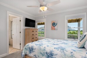 A bedroom with a bed, a ceiling fan, a TV, a window with a view, and a door leading to a bathroom. - Da Kine By Da C: Dog-Friendly, Oceanside Home in Ocean Sands, Private Heated Pool (Corolla)