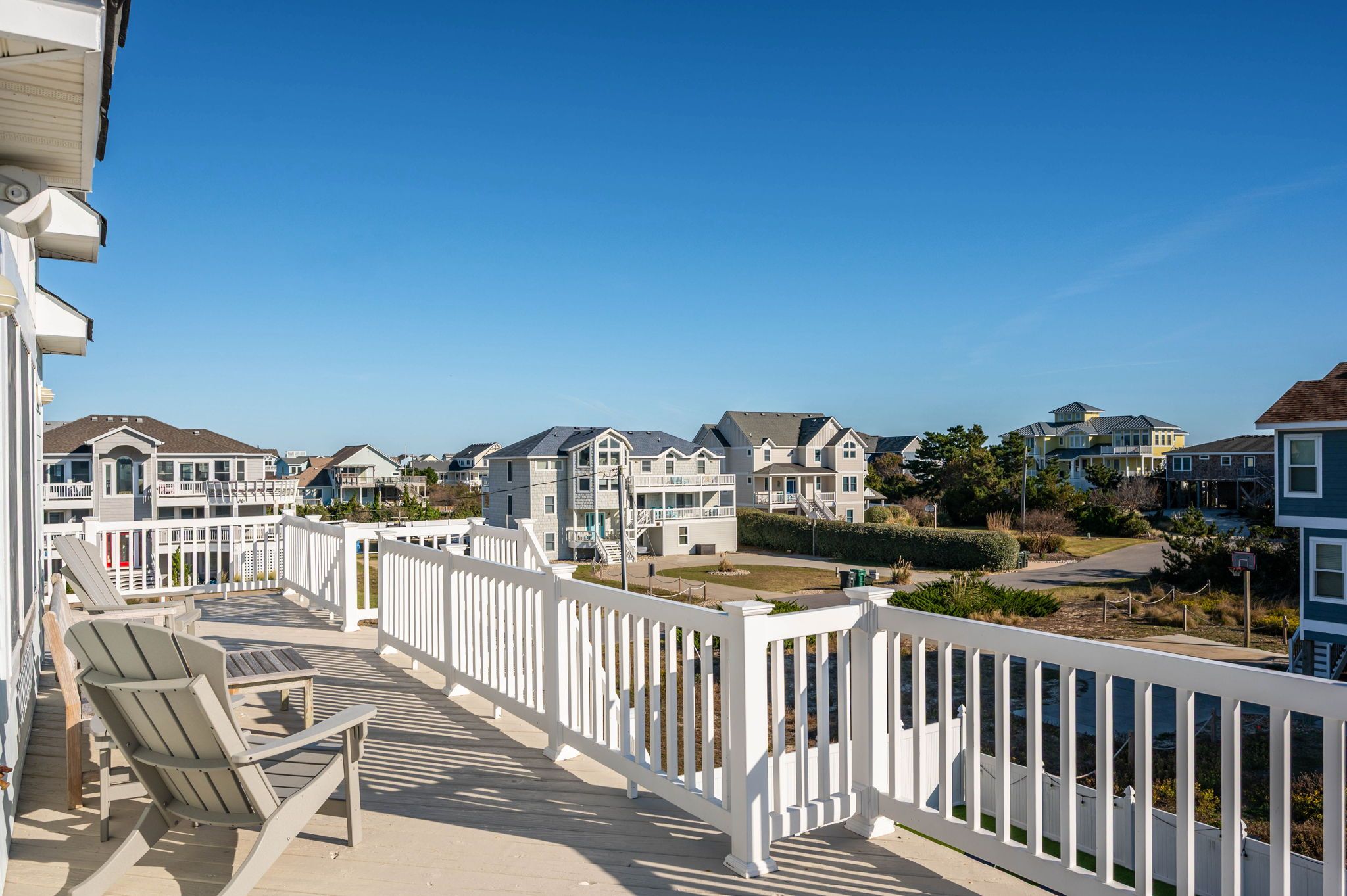A residential area with multiple two-story houses, a wooden deck with chairs, and a clear blue sky.