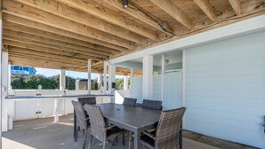 En udendørs terrasse med et træloft, et bord med stole og en hvid væg.