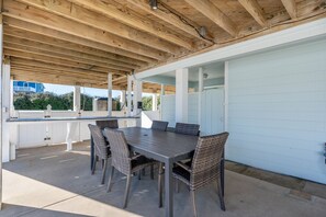 Un patio exterior con techo de madera, una mesa con sillas y una pared blanca.