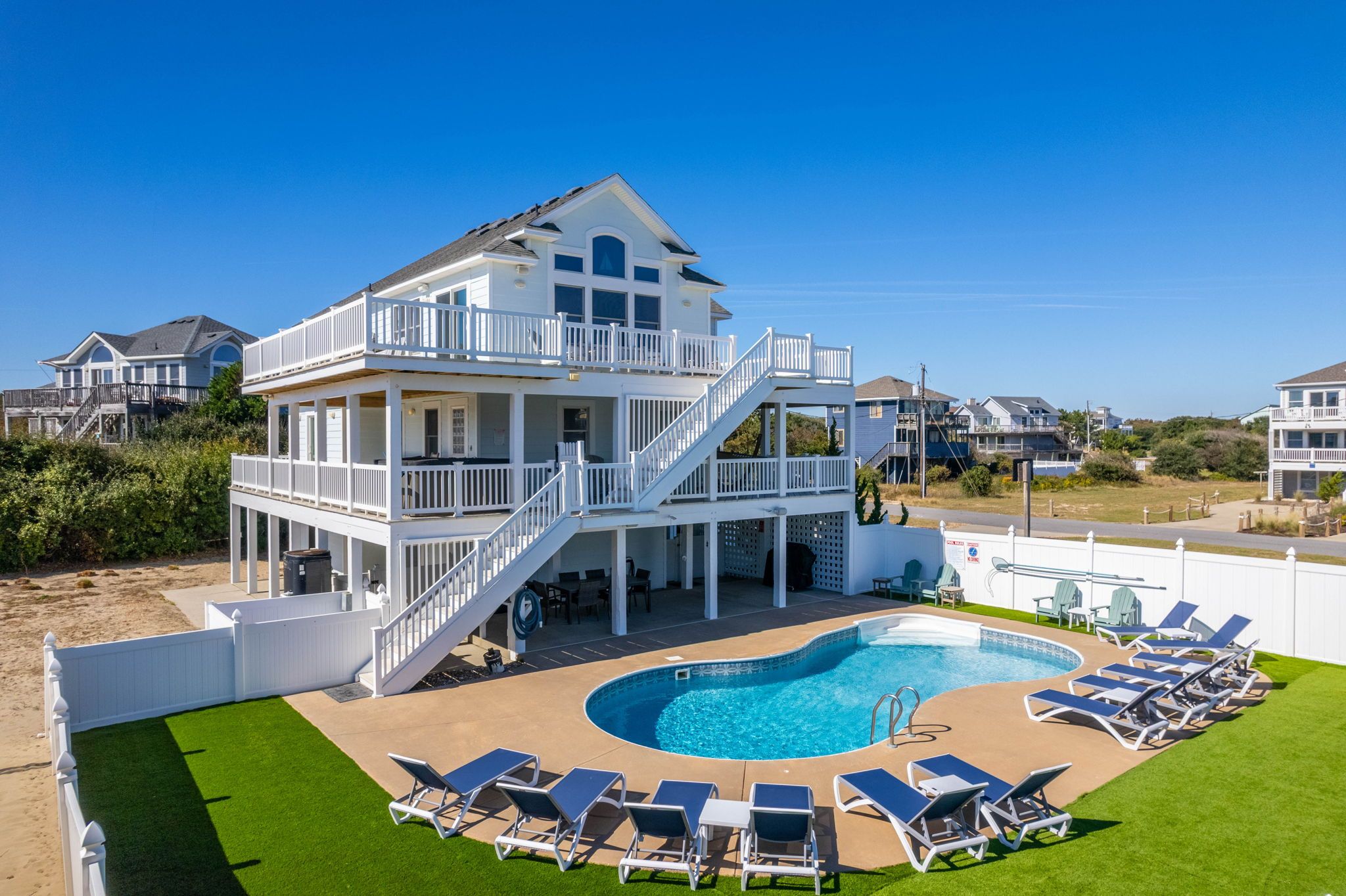 A two-story beachfront property with a swimming pool and sun loungers.