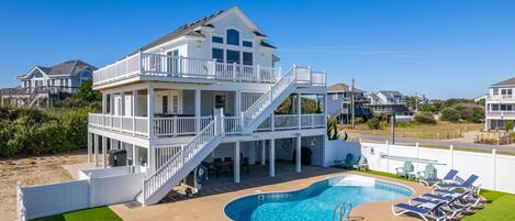 A two-story beachfront property with a swimming pool and sun loungers.