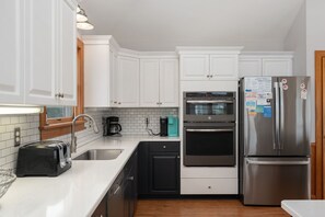 Una cocina moderna con armarios blancos, un refrigerador de acero inoxidable, horno integrado y una cafetera.