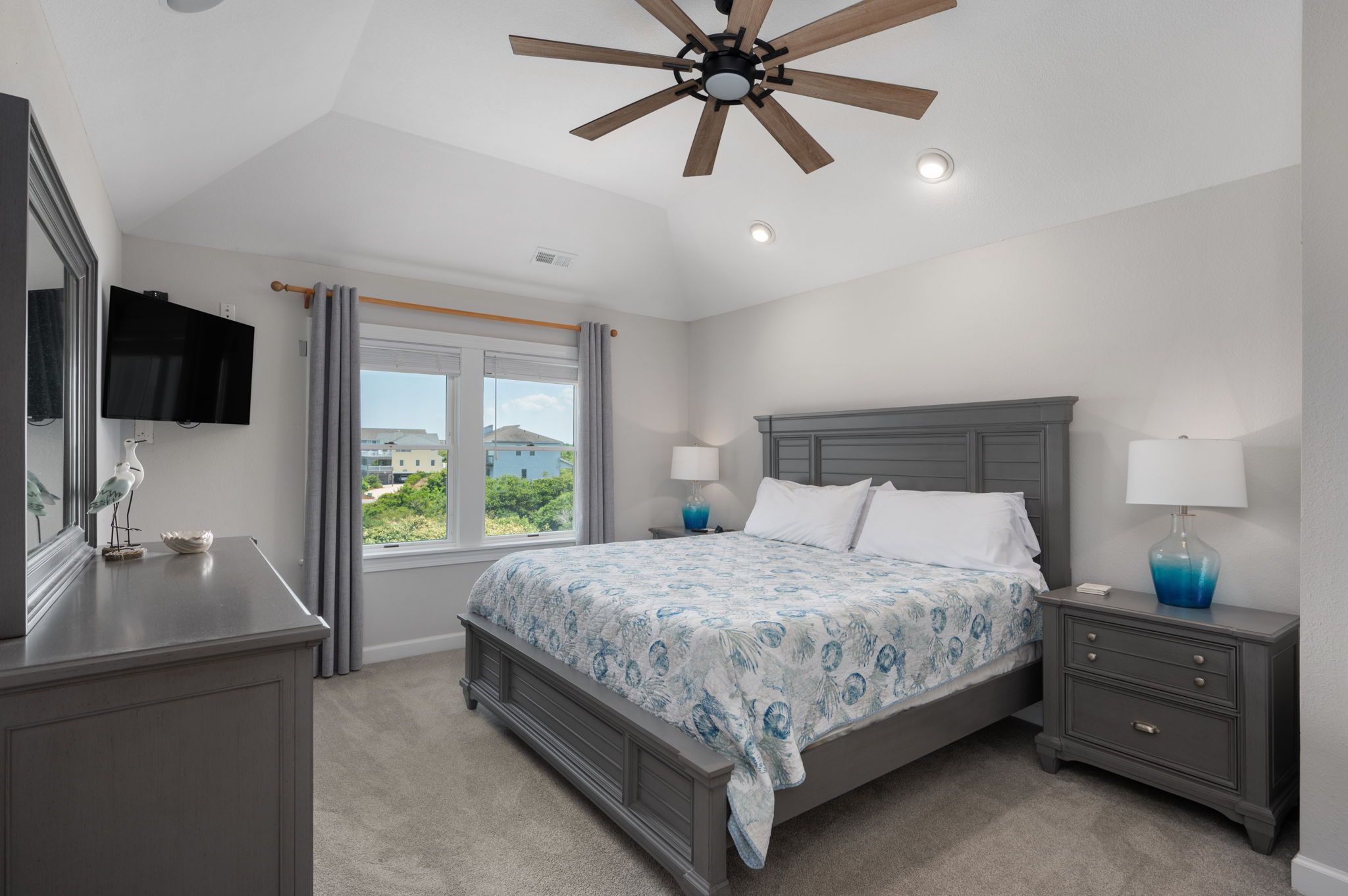 A bedroom with a bed, nightstands, a ceiling fan, a TV, and a window with curtains.