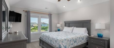 A bedroom with a bed, nightstands, a ceiling fan, a TV, and a window with curtains.