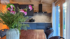A wooden dining table with a vase of flowers, a kitchen with blue cabinets, and a window with curtains. - 3 bedroom lovely home in Meijel (Meijel)