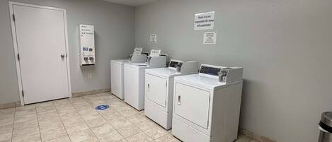 A laundry room with four washers and dryers, a soap and bleach softener dispenser, and a sign indicating the motel is not responsible for items left unattended.