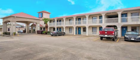 A motel with a central entrance, multiple balconies, and a parking area with several cars.