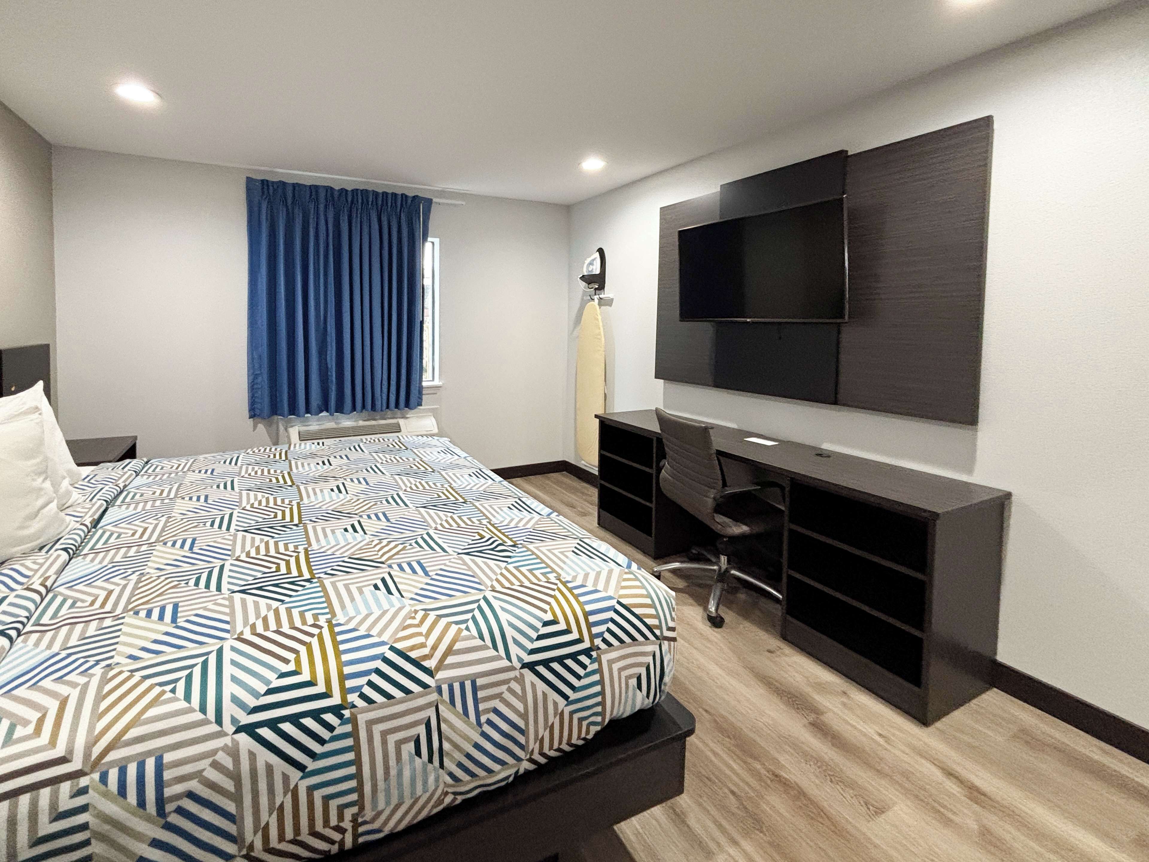 Una habitación de hotel moderna con una cama grande, un escritorio y un televisor de pantalla plana montado en la pared.