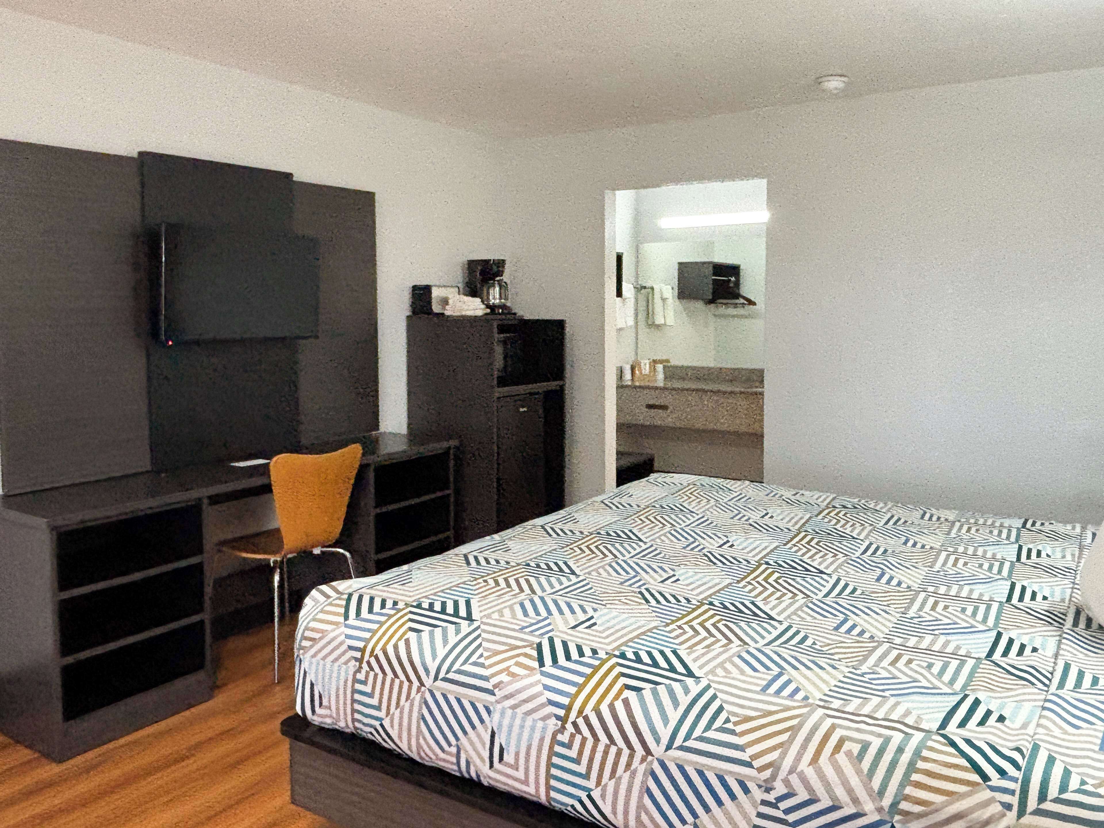 A hotel room with a bed, a desk, a chair, a television, and a mirror.
