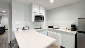 A modern kitchen with white cabinets, a microwave, a sink, and a refrigerator. - Studio 6 Sulphur, LA (Sulphur)