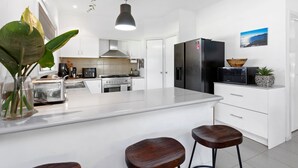 A modern kitchen with white cabinetry, a large island with stools, a black refrigerator, and a microwave. - The Beach Barn - Balnarring Beach (Balnarring Beach)