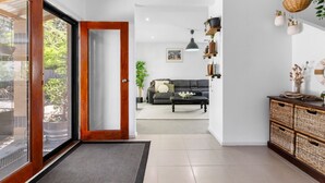 A modern living room with a grey sofa, a coffee table, and a dining area with wicker furniture. - The Beach Barn - Balnarring Beach (Balnarring Beach)