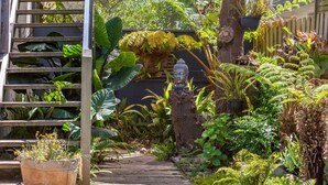 A garden pathway with a Buddha statue, lush greenery, and a wooden fence. - The Beach Barn - Balnarring Beach (Balnarring Beach)