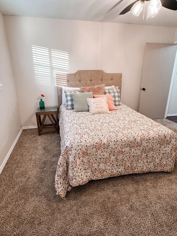A bedroom with a bed, a nightstand, a door, and a window with blinds.