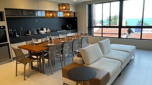 A modern kitchen with a dining area, a sofa, and a view of the sea.