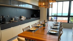 A modern kitchen with a dining area, large windows, and a view of the ocean.