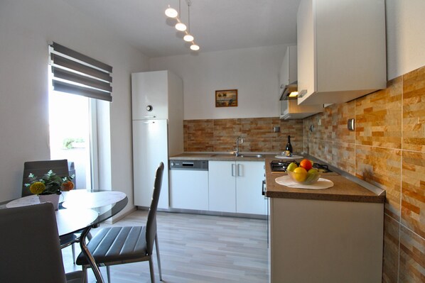 A modern kitchen with white cabinets, a built-in dishwasher, a gas stove, and a fruit bowl on the counter.