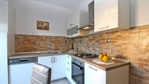Una cocina moderna con armarios blancos, un lavamanos de acero inoxidable, una estufa a gas y un microondas. Hay un frutero en la encimera y un cuadro en la pared.