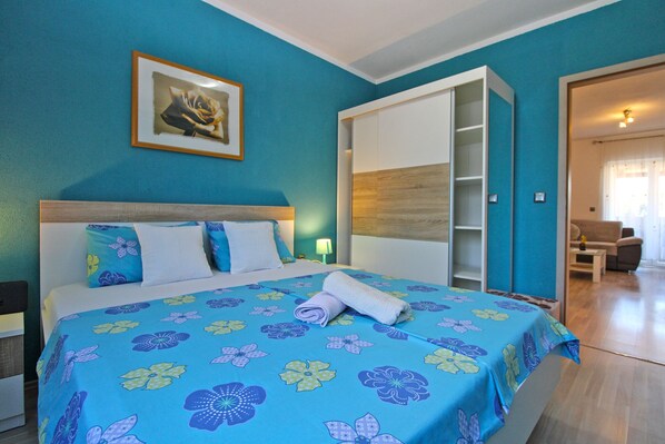 A hotel room with a bed, a nightstand, a painting, a wardrobe, and a seating area with a table and chairs.