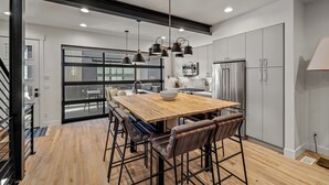 Une cuisine moderne avec une table à manger en bois, des tabourets de bar et des appareils électroménagers en acier inoxydable.