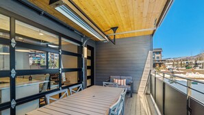 Un espace de restauration en plein air doté d’une terrasse en bois, d’une table avec des chaises et offrant une vue sur les bâtiments environnants.