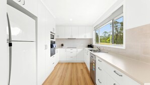 A modern kitchen with white cabinetry, a built-in oven, a microwave, and a dishwasher. There is a window providing a view of trees outside.