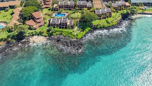 Luftaufnahme eines Küstenresorts mit mehreren Gebäuden, einer felsigen Küstenlinie und klarem türkisblauem Wasser.