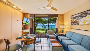 Ein Zimmer mit Esstisch für zwei Personen, einer Couch, einem Fernseher und Blick aufs Meer.