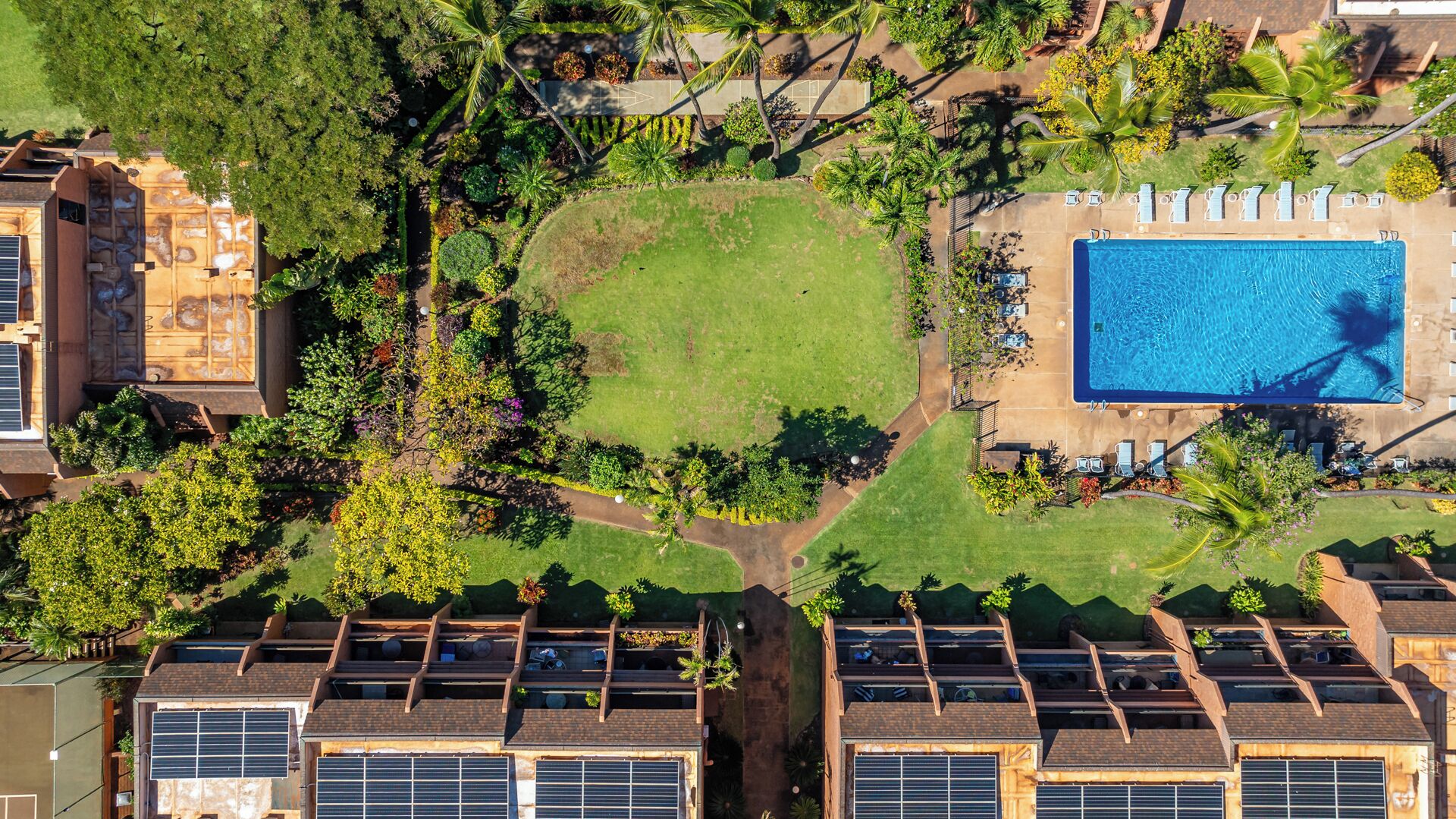 Vue aérienne d’un quartier résidentiel avec une piscine, des panneaux solaires sur les bâtiments et une pelouse bien entretenue.