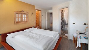 A hotel room with a large bed, a desk with a chair, and a bathroom visible through an open door. - Apartment 'Giulia' with Mountain View, Shared Garden and Balcony (Canazei)