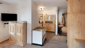A compact kitchen with wooden cabinets, a built-in stove, and a television. - Apartment 'Giulia' with Mountain View, Shared Garden and Balcony (Canazei)