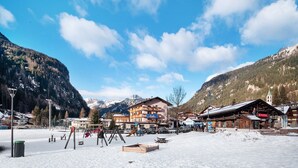A snow-covered outdoor area with a playground, buildings, and mountains in the background. - Apartment 'Giulia' with Mountain View, Shared Garden and Balcony (Canazei)