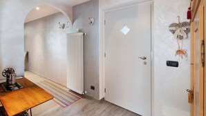 A hallway with a radiator, a door with a peephole, and a table with a striped rug. - Apartment 'Giulia' with Mountain View, Shared Garden and Balcony (Canazei)