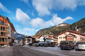 A mountain resort with wooden buildings, a parking lot, and a view of snow-capped mountains. - Apartment 'Giulia' with Mountain View, Shared Garden and Balcony (Canazei)