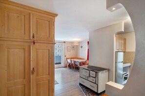 A kitchen with wooden cabinets, a dining area with a table and chairs, and a small refrigerator. - Apartment 'Giulia' with Mountain View, Shared Garden and Balcony (Canazei)