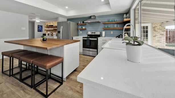 Een moderne keuken met een centraal eiland, houten barstoelen, een inbouwoven en een groot raam met uitzicht op de omgeving.
