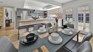 Een moderne keuken met een centraal eiland, een eethoek met een tafel voor vier personen en uitzicht op de achtertuin door grote schuifdeuren.