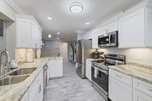 A modern kitchen with white cabinets, stainless steel appliances, and a marble countertop. - Cape Coral VIP Heated Pool, Spa, Direct access Boat lift, Gameroom, Scooters (Cape Coral)