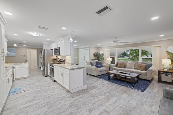 Una cocina moderna con armarios blancos, una isla central y una zona de comedor con sofá y mesa de centro.