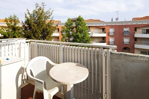Ein Balkon mit weißem Stuhl und Tisch, einem weißen Zaun und Gebäuden im Hintergrund.
