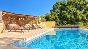 Une piscine avec des chaises longues et une structure recouverte de chaume.