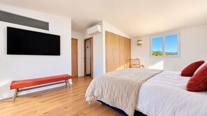 Une chambre avec un lit, un banc, une télévision et une fenêtre donnant sur un beau paysage.