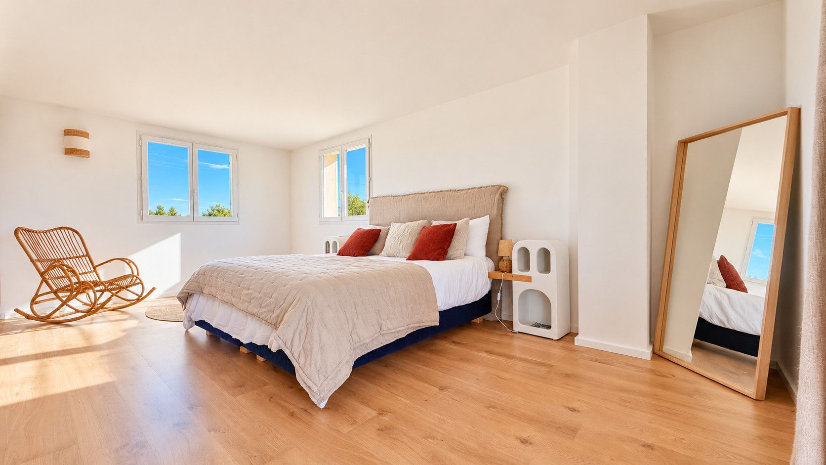 A bedroom with a bed, a rocking chair, a bedside table, and a mirror.