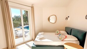 Une chambre avec un lit, une petite table, un miroir et une vue sur une piscine à l’extérieur.